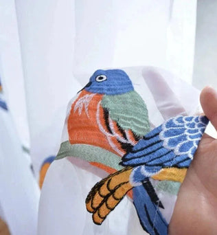 Image d'un motif délicatement brodé représentant un oiseau coloré sur un fond clair. Le design vibrant inclut des nuances de bleu, orange et vert, offrant une touche artistique et élégante pour la décoration intérieure. Parfait pour apporter une ambiance naturelle et chaleureuse à votre espace de vie. Idéal pour les amateurs de motifs animaliers et de décoration unique.