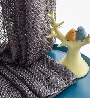 Rideau décoratif gris avec motif texturé, mis en valeur sur une table bleu canard, accompagné d'un élégant porte-bijoux en forme de branche, accueillant deux oiseaux colorés. Parfait pour ajouter une touche d'élégance et de modernité à votre intérieur. Ideal pour le salon ou la chambre.