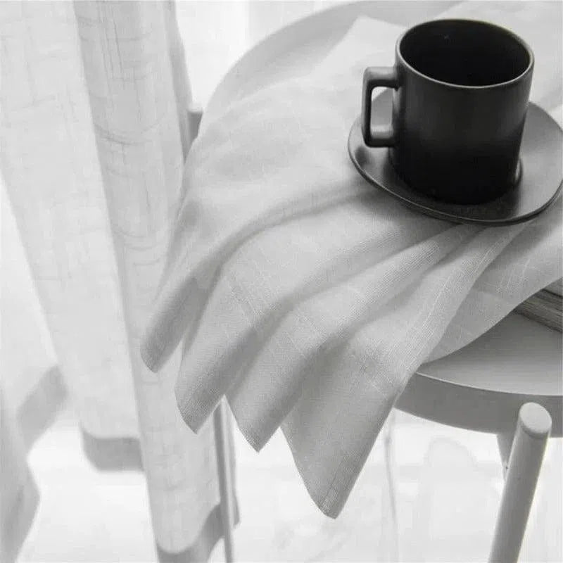 Tasse à café noire élégante sur une table blanche, posée sur une nappe immaculée, avec des rideaux lumineux en arrière-plan. Idéale pour une décoration moderne et minimaliste.