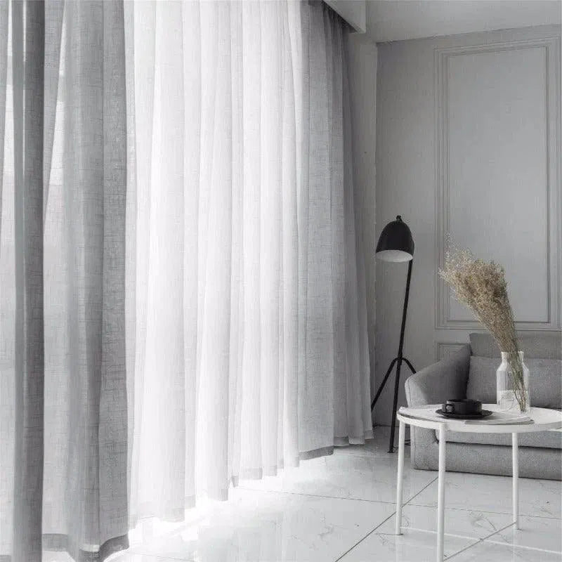 Rideaux blancs élégants pour salon moderne avec déco minimaliste, chaise grise confortable, lampe élégante et table basse design. Idéal pour un intérieur lumineux et contemporain.