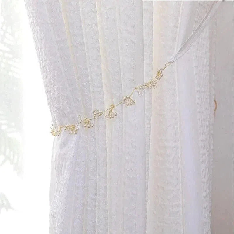 Rideau blanc élégant avec embrasse délicate ornée de petites perles, idéal pour embellir votre intérieur tout en laissant filtrer une douce lumière naturelle. Convient parfaitement pour des salons raffinés ou des chambres apaisantes.