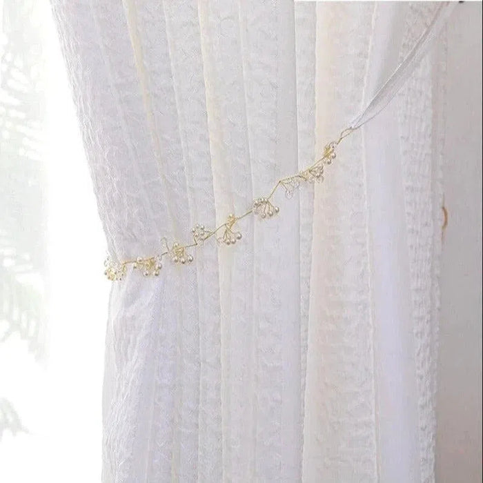 Rideau blanc élégant avec embrasse délicate ornée de petites perles, idéal pour embellir votre intérieur tout en laissant filtrer une douce lumière naturelle. Convient parfaitement pour des salons raffinés ou des chambres apaisantes.