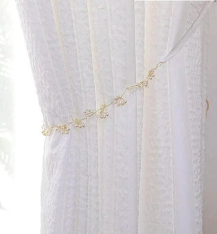 Rideau blanc élégant avec embrasse délicate ornée de petites perles, idéal pour embellir votre intérieur tout en laissant filtrer une douce lumière naturelle. Convient parfaitement pour des salons raffinés ou des chambres apaisantes.