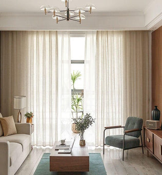 Salon moderne avec un canapé confortable et fauteuil élégant face à une table basse design. Rideaux en fond pour un éclairage naturel optimal. Décoration intérieure épurée avec plantes et accessoires modernes, créant une ambiance chaleureuse et accueillante. Lustre chic pour une touche d'élégance. Idéal pour des inspirations déco actuelles.