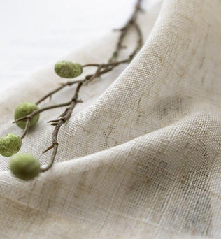 Image d'un tissu naturel drapé, accentué par une branche avec des baies vertes, créant une ambiance végétale et organique. Ce produit est parfait pour une décoration intérieure inspirée par la nature.