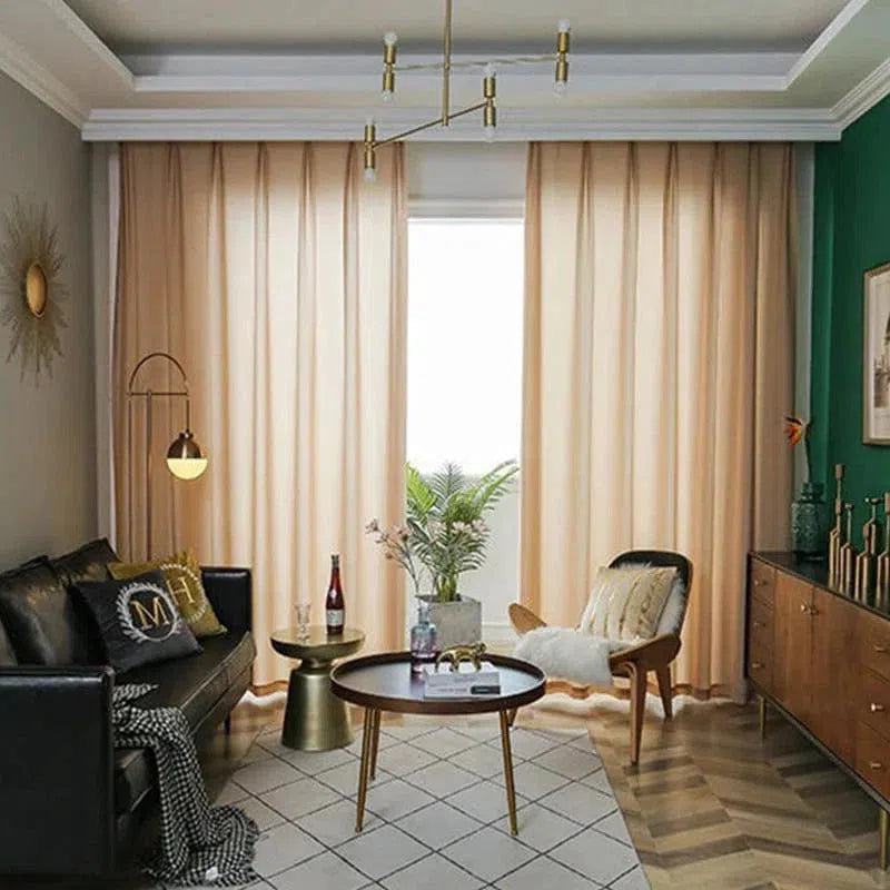 Salon moderne et élégant avec canapé en cuir noir, table basse ronde en bois et chaises d'appoint. Rideaux beiges devant une grande fenêtre apportant une lumière naturelle abondante. Décoration intérieure sophistiquée avec des plantes vertes et des lampes de style contemporain, parfait pour une ambiance chaleureuse et accueillante.