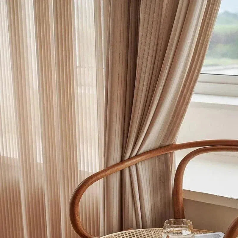 Rideaux élégants beige suspendus dans un salon lumineux, avec chaise au design épuré en premier plan à proximité d'une fenêtre. Décoration moderne et apaisante idéale pour sublimer l'intérieur de votre maison.