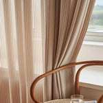 Rideaux élégants beige suspendus dans un salon lumineux, avec chaise au design épuré en premier plan à proximité d'une fenêtre. Décoration moderne et apaisante idéale pour sublimer l'intérieur de votre maison.