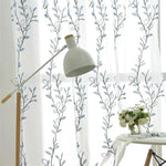 Rideaux décoratifs avec motifs floraux bleu et blanc, parfaits pour illuminer une pièce et ajouter une touche de style moderne. Accessoire idéal pour salons et chambres à coucher, qui apporte une ambiance fraîche et élégante. Lampadaire moderne en arrière-plan pour un éclairage doux et harmonieux. Vases avec fleurs blanches pour un décor raffiné et naturel.