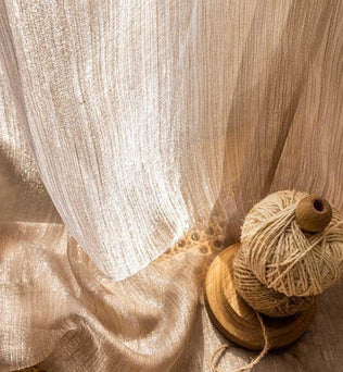 Voilage élégant et lumineux près d'une bobine de fil beige, idéal pour sublimer la décoration intérieure avec une touche chic et naturelle. Parfait pour les salons ou chambres, il apporte une ambiance douce et apaisante grâce à sa teinte chaleureuse et ses reflets scintillants.