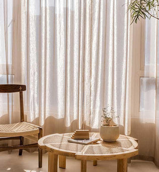 Rideaux légers et élégants habillant une fenêtre, illuminant un coin détente avec une table basse au design épuré et une chaise rustique. Ambiance chaleureuse et accueillante pour une décoration intérieure moderne et naturelle. Plante d'intérieur ajoutant une touche de verdure apaisante.