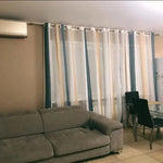 Canapé confortable gris pour salon moderne, positionné près d'une table à manger avec des chaises noires élégantes. Les rideaux rayés apportent une touche de style et d'élégance à la pièce lumineuse, créant une atmosphère accueillante et contemporaine. Idéal pour décorer avec goût tout espace de vie.