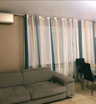 Canapé confortable gris pour salon moderne, positionné près d'une table à manger avec des chaises noires élégantes. Les rideaux rayés apportent une touche de style et d'élégance à la pièce lumineuse, créant une atmosphère accueillante et contemporaine. Idéal pour décorer avec goût tout espace de vie.