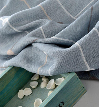 Étoffe à motif à carreaux gris-bleu drapée à côté d'une boîte en bois turquoise contenant des petits coquillages blancs.