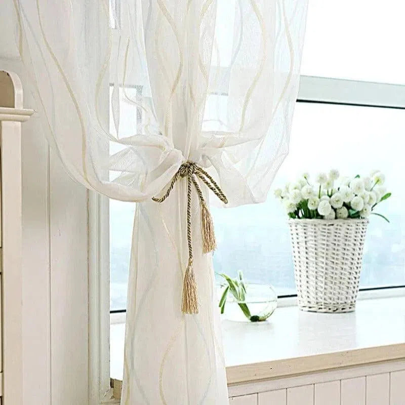 Voilage élégant pour fenêtre avec embrasse décorative, apportant une touche raffinée à votre intérieur. Idéal pour tamiser la lumière tout en préservant l'intimité. Parfait pour les salons ou chambres modernes. Panier de fleurs blanches en arrière-plan ajoutant une ambiance chaleureuse.