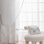 Chaise moderne et élégante devant une grande fenêtre avec rideaux translucides, offrant une ambiance lumineuse et épurée. Un coussin décoratif ajoute une touche artistique et confortable à l'ensemble de la pièce. Style minimaliste et raffiné idéal pour un salon ou une chambre contemporaine.