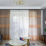 Paire de rideaux élégants aux tons neutres, habillant une grande baie vitrée dans un salon moderne. Les motifs ajourés ajoutent une touche décorative subtile, tandis que le design élégant procure une ambiance chaleureuse. Parfait pour apporter une lumière douce et tamisée dans votre espace de vie.