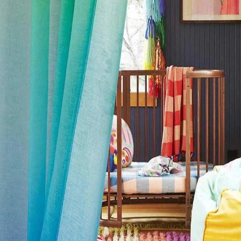 Chambre de bébé colorée avec un lit à barreaux en bois. Les rideaux turquoise ajoutent une touche lumineuse à la pièce, tandis que la décoration multicolore crée une ambiance joyeuse. Idéal pour un espace moderne et ludique, parfait pour stimuler l'imagination des tout-petits.