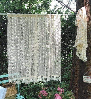 Rideau décoratif crochet beige suspendu dans un jardin verdoyant, idéal pour apporter une touche bohème à votre intérieur. Style artisanal avec franges, parfait pour créer une ambiance cosy et élégante. Parfait pour les salons, chambres ou espaces extérieurs couverts. Accessoire tendance pour personnaliser vos espaces avec charme et authenticité.
