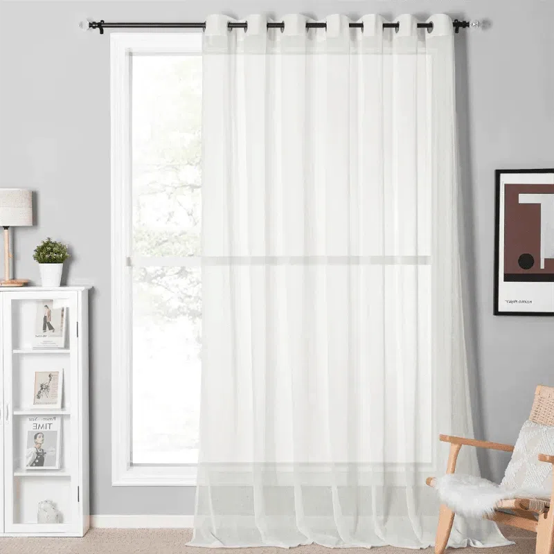 Rideau transparent blanc pour salon moderne, suspendu à une tringle noire devant une fenêtre lumineuse. Décoration intérieure épurée avec fauteuil, lampe sur petite étagère, et cadre artistique. Idéal pour une ambiance lumineuse et élégante.