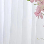 Rideau blanc translucide suspendu, offrant une ambiance lumineuse et élégante, idéal pour la décoration intérieure moderne. Fleurs roses délicates visibles en arrière-plan, ajoutant une touche de sophistication naturelle.