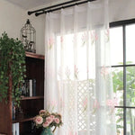 Voilage floral pour fenêtre, décoratif avec motifs élégants roses et verts. Idéal pour une ambiance lumineuse et naturelle dans le salon. Se combine parfaitement avec une bibliothèque en bois et des plantes d'intérieur. Accessoire décoratif parfait pour améliorer la luminosité et le style de votre espace de vie.